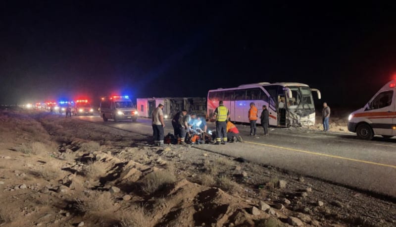 Escena de accidente nocturno en carretera con tráiler y autobús dañados iluminados por luces de emergencia