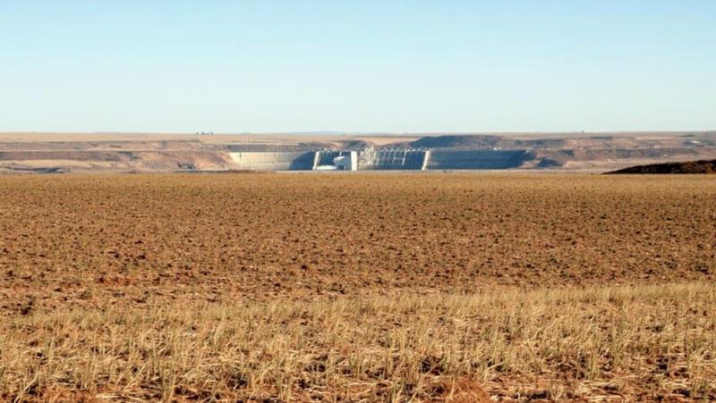 Campos agrícolas secos con una presa visible en el horizonte bajo el cielo despejado del norte de Chihuahua