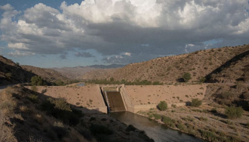 Presa con nivel bajo de agua en un valle árido del norte de México, con cerros secos al fondo y nubes de tormenta en el cielo