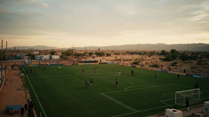 Campo de fútbol en construcción con equipos de iluminación y materiales de instalación en las orillas del terreno