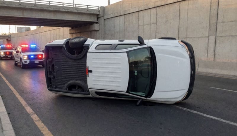 Camioneta volcada sobre el pavimento con luces de emergencia parpadeando al fondo en un puente urbano