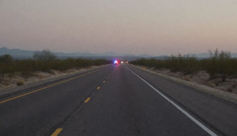 Carretera desértica del estado de Chihuahua con luces de emergencia destellando en la distancia al atardecer
