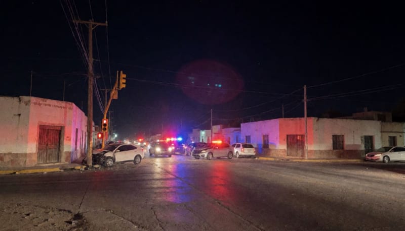 Escena de choque nocturno con dos vehículos dañados y poste de servicios caído en una intersección urbana