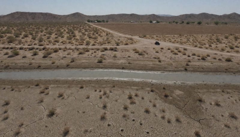 Vista aérea de una presa con poca agua, orillas de lodo agrietado y campos agrícolas secos en el desierto
