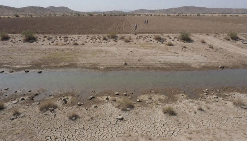 Vista aérea de un embalse casi seco con tierra agrietada en la orilla y campos de cultivo áridos al fondo