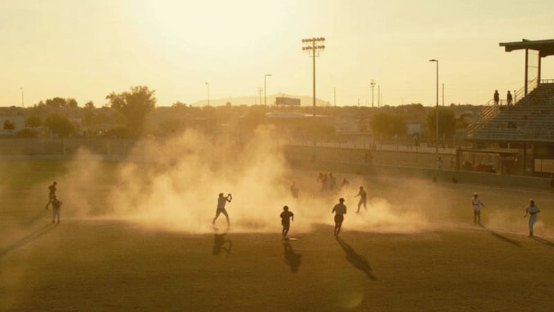 Jugadores veteranos compitiendo en el diamante bajo la luz dorada del atardecer en un campo de beisbol del desierto