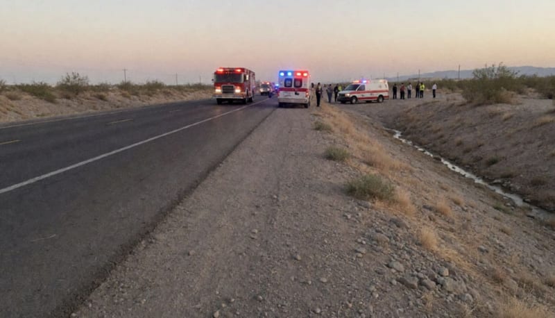 Carretera del desierto al atardecer con unidades de emergencia estacionadas junto a un dren