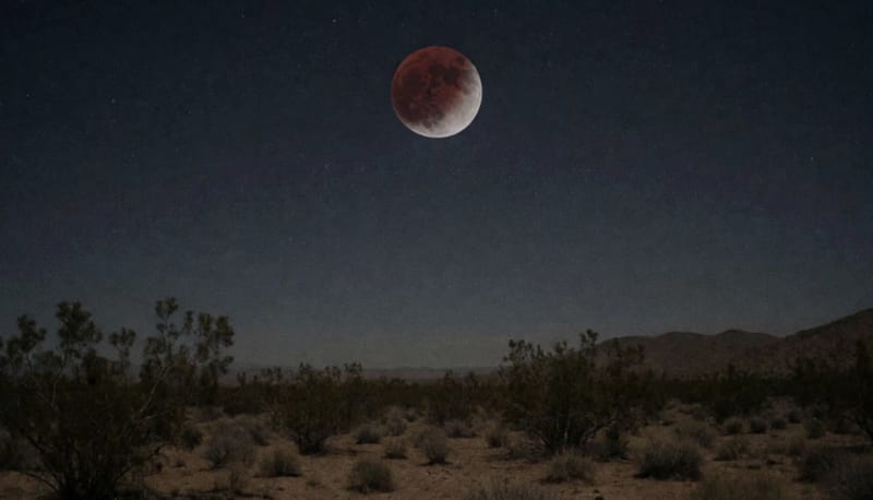 Luna teñida de rojo oscuro casi completamente cubierta por la sombra terrestre sobre el cielo nocturno del desierto