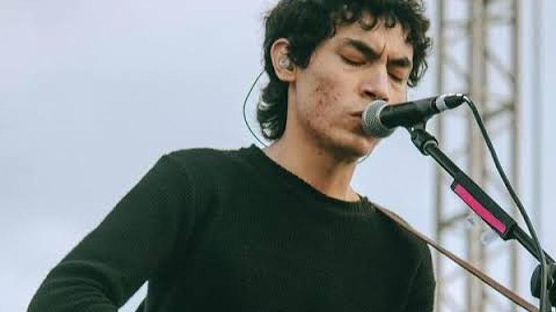 Ed Maverick canta frente al micrófono con su guitarra acústica durante un concierto al aire libre