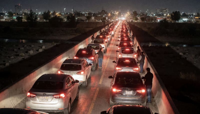 Larga fila de autos detenidos de noche sobre un puente con luces rojas traseras y la ciudad iluminada al fondo