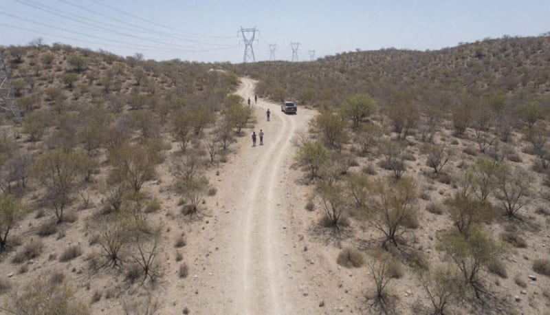 Terreno árido y accidentado con torres eléctricas al fondo y una camioneta lejana sobre un camino de terracería