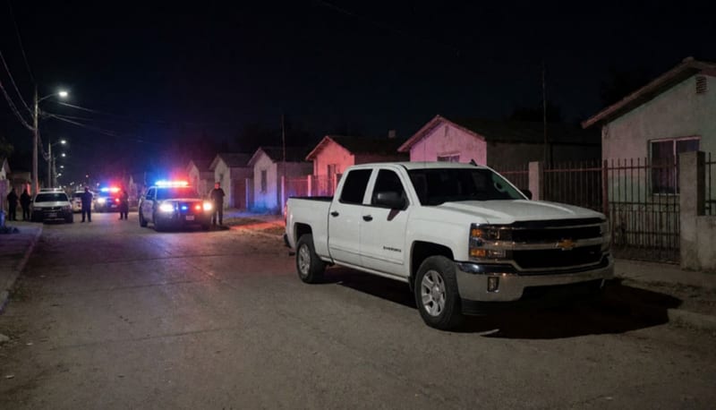 Camioneta blanca estacionada en una calle residencial nocturna con luces policiales de fondo