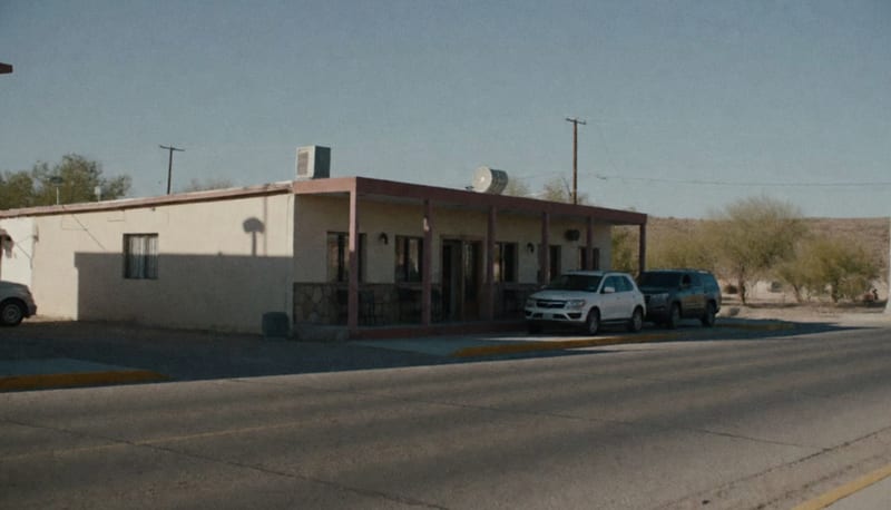 Fachada de un hotel en una ciudad desértica del norte de México con estacionamiento y cerros al fondo