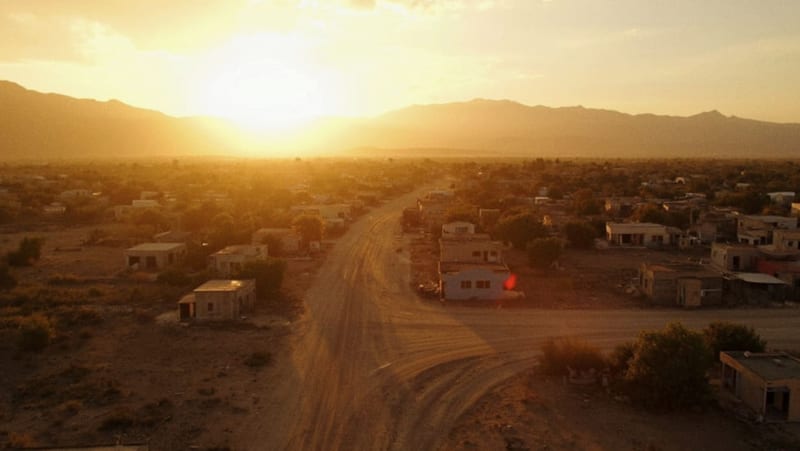Casas de concreto en formación sobre terreno árido al atardecer, montañas al fondo