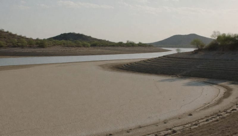 Vaso de una presa casi vacío, con el suelo agrietado en primer plano y un hilo de agua al fondo