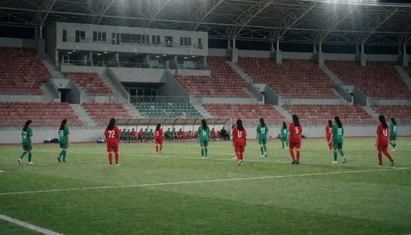 Partido de futbol femenil juvenil visto desde lejos en un estadio iluminado