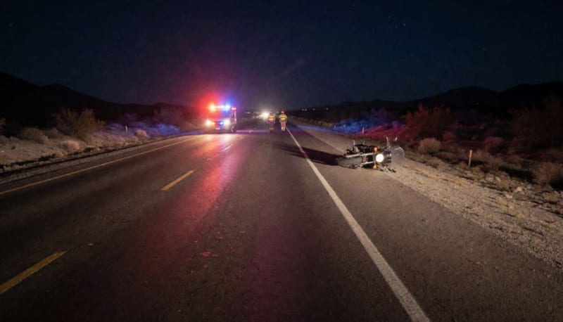 Motocicleta caída a la orilla de una carretera desértica de noche con luces rojas y azules de emergencia al fondo