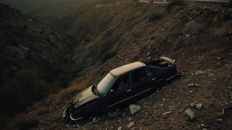 Automóvil dañado en el fondo de un barranco rocoso bajo la carretera al atardecer
