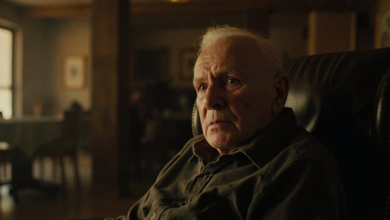Hombre de avanzada edad sentado en un interior, con expresión contemplativa y luz natural suave