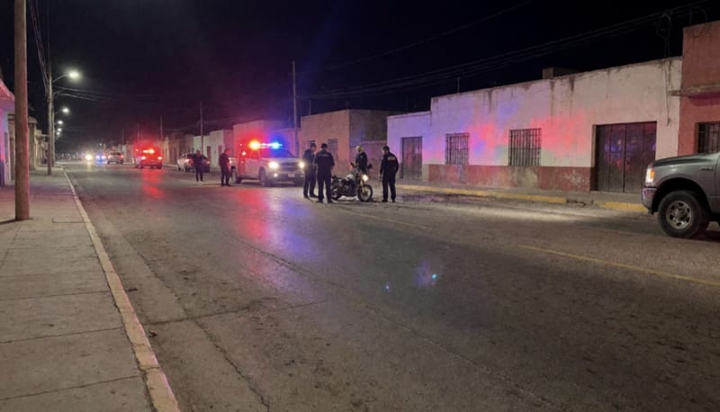 Motocicleta incendiada sobre una calle con luces de emergencia parpadeando en la madrugada