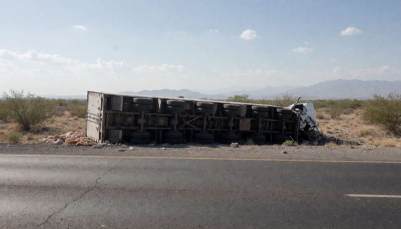 Tráiler volcado sobre la carretera en el desierto chihuahuense con carga dispersa alrededor